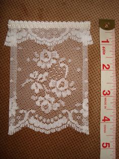 a piece of white lace next to a measuring ruler on a brown cloth with an embroidered design