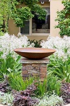 a stone bowl sitting on top of a planter in the middle of a garden