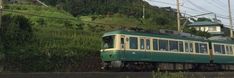 a green and yellow train traveling down tracks next to a lush green hillside