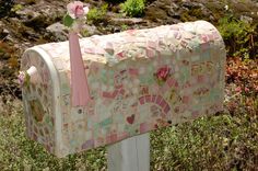 a mailbox decorated with mosaic tiles and pink ribbon tied to the front, sitting in some grass