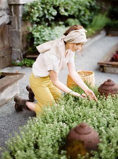 a woman kneeling down to pick up some plants