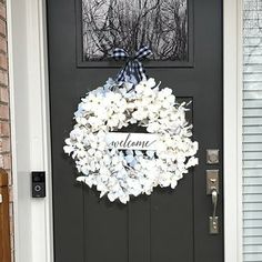 a black door with a welcome sign and white flowers hanging on the front door handle