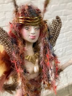 a close up of a doll with feathers on it's head and hair around her body