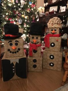 three snowmen made out of cardboard boxes in front of a christmas tree with lights