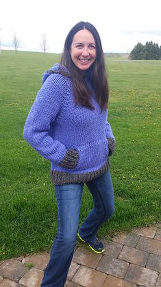 a woman standing in the grass with her hands on her hips wearing a blue sweater