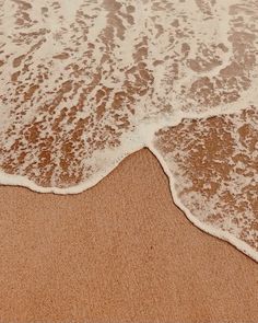 an ocean wave rolls in on the sand at the beach with white foamy waves