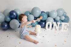 a baby sitting on the floor with a cake in front of it and balloons behind him