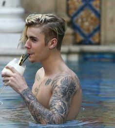 a man with tattoos drinking from a bottle in the water while holding a straw to his mouth