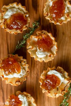 small tarts filled with sauce and whipped cream on top of a wooden table next to rosemary sprigs