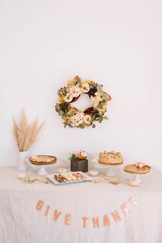 a table topped with cakes and pies on top of a white table cloth next to a wreath