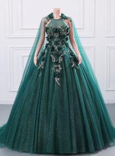 Roses are green in this spectacular prom dress that exudes sophistication and charm. The gown features a high neckline with beautifully detailed floral appliques that flow down the bodice, creating a whimsical and romantic look. The fitted bodice enhances your natural curves, while the full skirt adds a touch of drama and elegance. The shimmering emerald fabric catches the light perfectly, making you sparkle with every step. The dress also includes a matching cape that drapes gracefully over your shoulders, adding an element of mystery and allure. This gown is ideal for those who wish to make a bold and unforgettable statement at their prom. Embrace the enchantment and grace of this exquisite dress and let your inner beauty shine. Step into this gown and make your special night a magical a Quinceanera Dresses Elegant, Quinceanera Dresses Green, Backless Ball Gown, Ball Gown Quinceanera Dresses, Green Ball Gown, Dress Quinceanera, Sparkly Prom Dresses, Blue Ball Gowns, Floral Prom Dresses