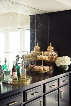 a black counter topped with lots of bottles and vases filled with flowers next to a mirror