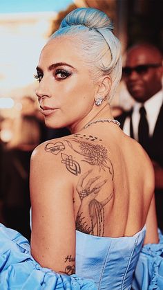 a woman with blue hair and tattoos on her back is looking off to the side