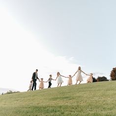 a group of people walking across a lush green field next to each other on top of a grass covered hillside