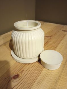 a white candle holder sitting on top of a wooden table next to a small container