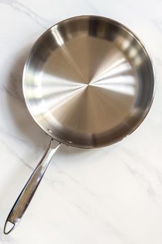 a stainless steel frying pan on a white marble counter top with a silver handle