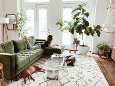 a woman laying on top of a green couch in a living room next to a dog