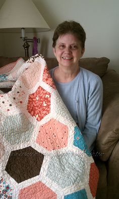 a woman sitting on a couch holding up a quilted blanket with hexagons