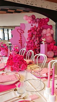 a table set for a party with pink decorations and balloons on the wall behind it