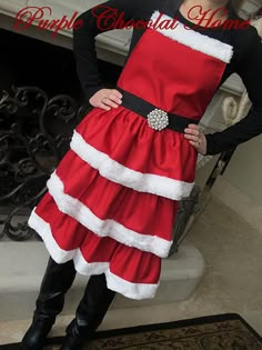 a woman wearing a santa claus costume standing in front of a fireplace with her hands on her hips