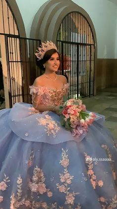 a woman in a blue ball gown with flowers on the skirt and tiara is smiling at the camera