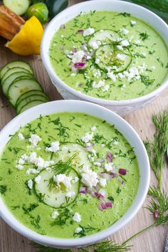 two white bowls filled with green soup next to cucumbers