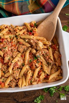 a white casserole dish filled with pasta and meat, garnished with parsley