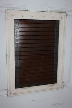 an old window with blinds on the side of it in a white wall, next to a toilet