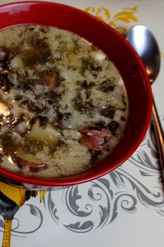 a red bowl filled with soup on top of a table next to spoons and utensils