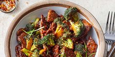 a bowl filled with meat and broccoli on top of a table next to silverware