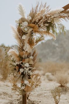 an arrangement of dried flowers and feathers on a wooden stand in the middle of nowhere