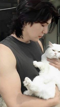 a man holding a white cat in his arms and looking at the camera while wearing a black tank top