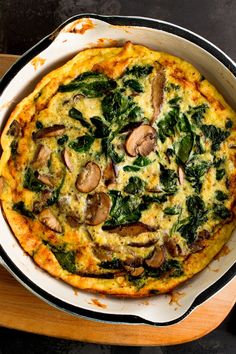 an omelet with spinach and mushrooms in a pan on a wooden tray