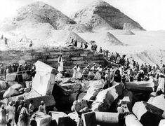 an old black and white photo of people in the desert with piles of logs, barrels and other items