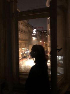 a person standing in front of a window looking out at the street outside and lights on