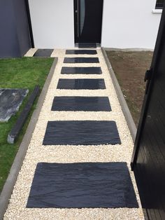 a black door is open on a gravel path that leads to a white building and green grass