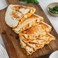 four quesadillas stacked up on a cutting board next to a bowl of greens