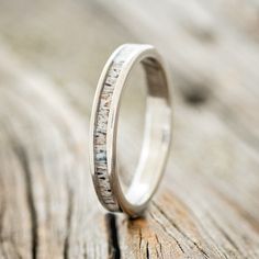 a wedding ring with white gold and silver inlays on a wooden surface,