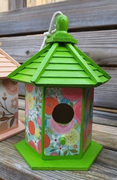 two colorful bird houses sitting on top of a wooden bench next to another birdhouse