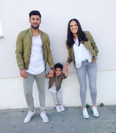 a man and woman holding hands while standing next to a little boy in front of a white wall