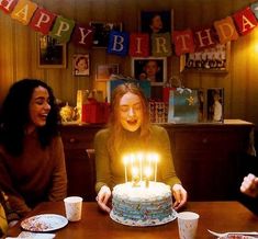 three women sitting at a table with a birthday cake and candles in front of them