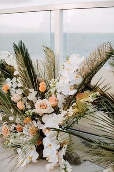 a vase filled with white and orange flowers on top of a table next to a window