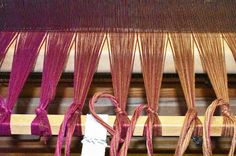 some pink and purple yarn hanging from a loom