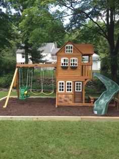 a wooden playset with a green slide and swing set in the middle of a yard