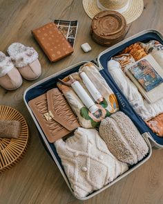 an open suitcase filled with clothing and shoes on top of a wooden floor next to wicker baskets