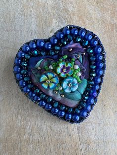 a heart - shaped brooch with blue beads and flowers on it sits on a wooden surface