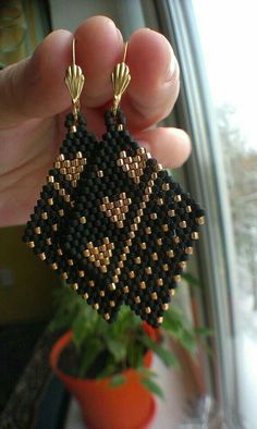 a hand holding up a pair of black and gold beaded earrings on top of a potted plant