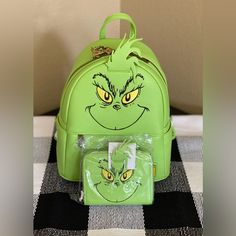 the grin face backpack is green with yellow eyes and has a clear plastic bag in front of it