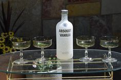 an assortment of wine glasses sitting on a glass table with a bottle of absouu vanilla