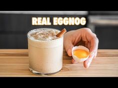 a person holding an egg in front of a drink on a table with the words real eggnog written above it